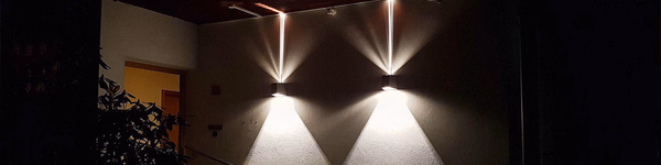Zwei moderne Wandleuchten beleuchten eine Hausfassade bei Nacht mit symmetrischen Lichtkegeln nach oben und unten